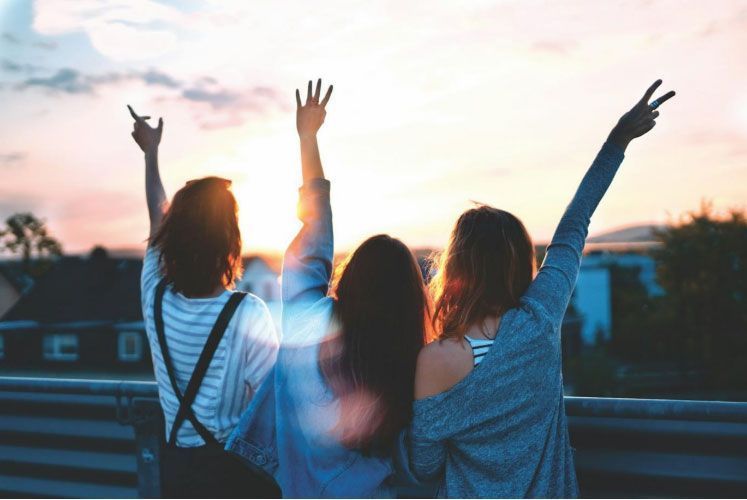 Three women are standing on a balcony with their arms in the air.