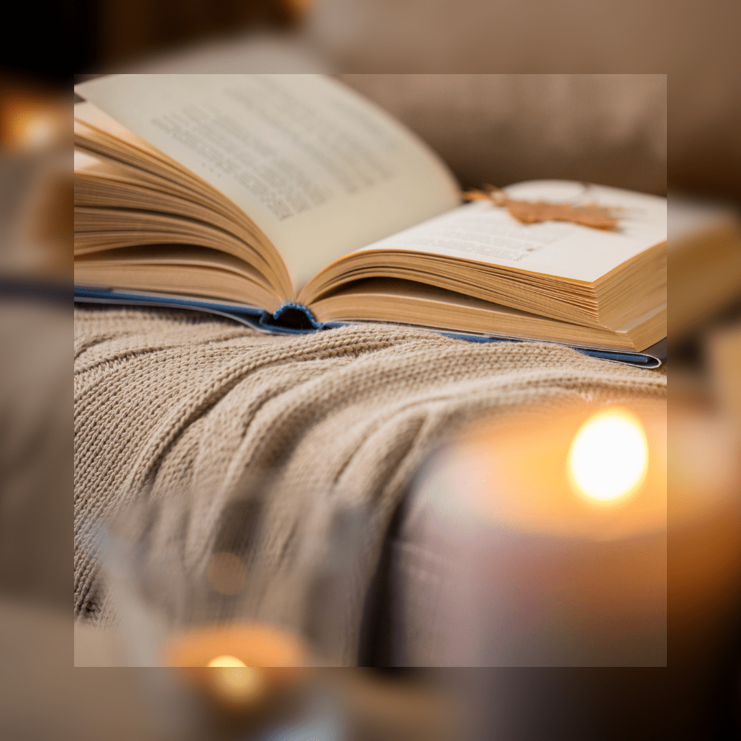 Open book on a beige blanket, with a candle in soft focus in the foreground.