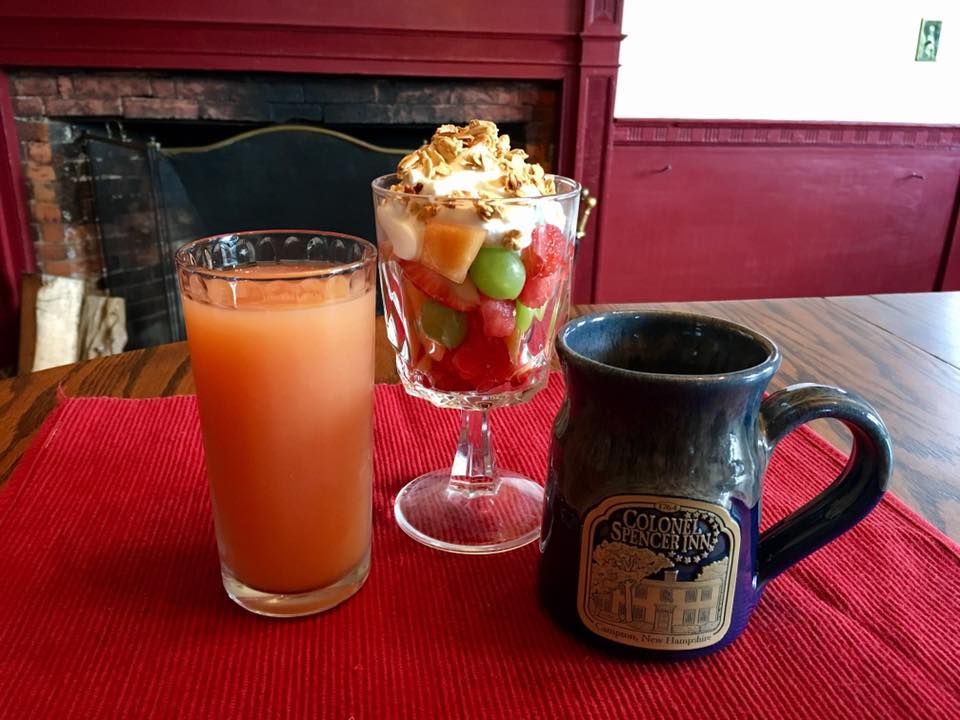 A glass of orange juice a bowl of fruit and a mug on a table