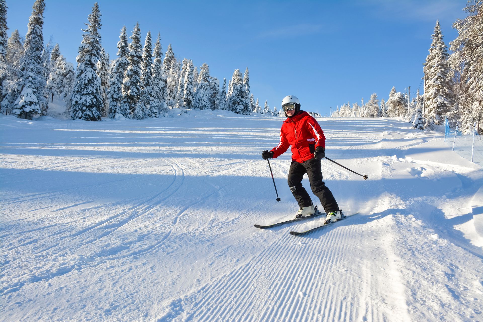 A man in a red jacket is skiing down a snow covered slope.