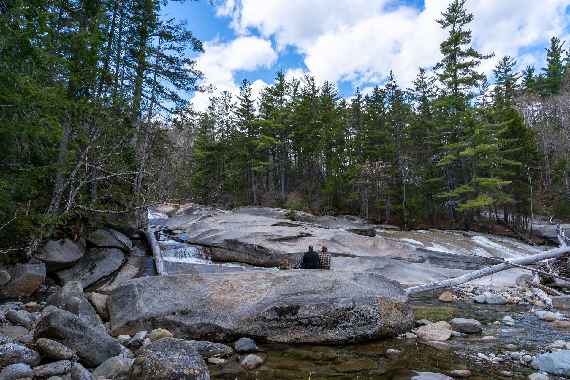 A man is sitting on a rock near a river in the woods.