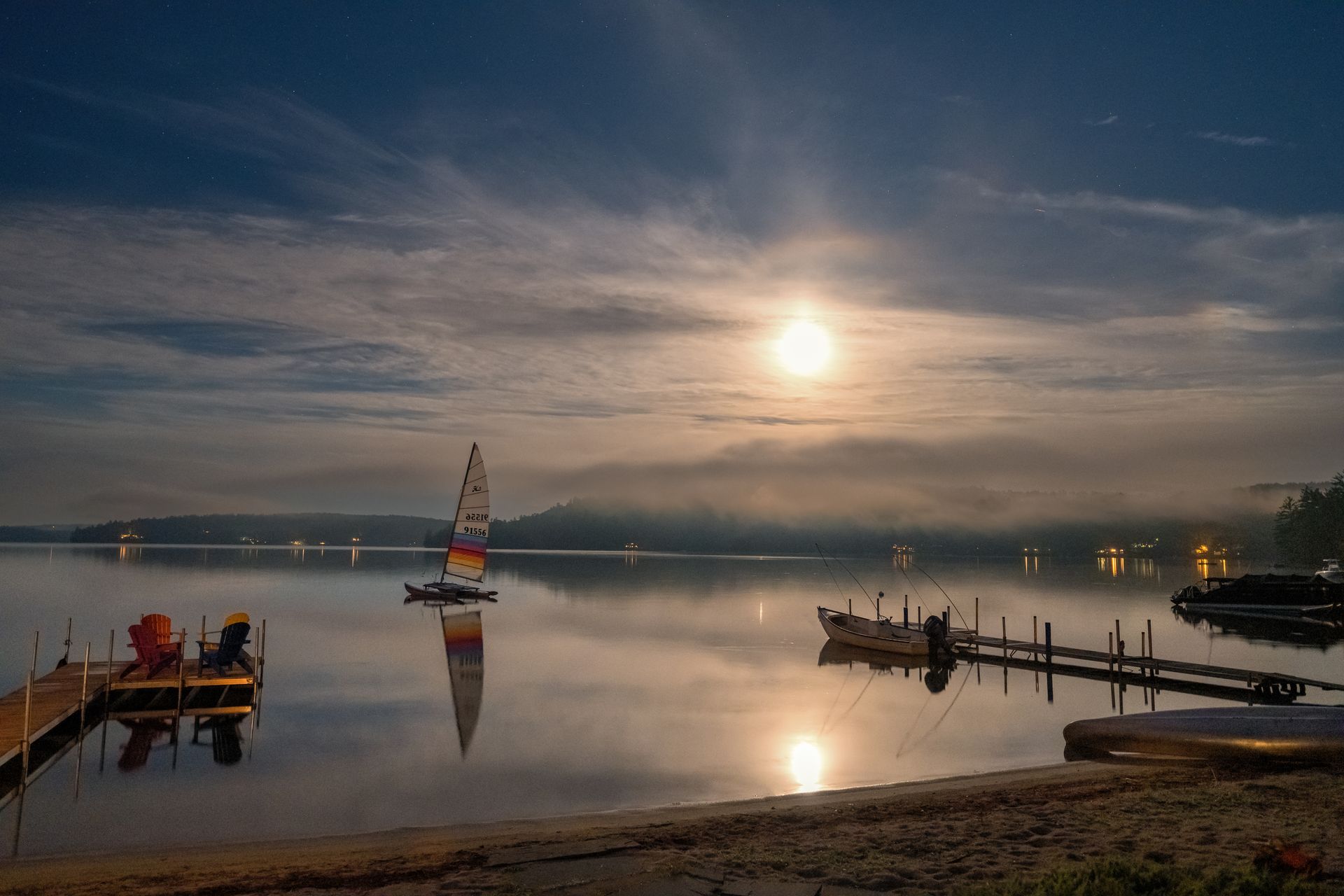 A full moon is shining over a lake with boats in the water