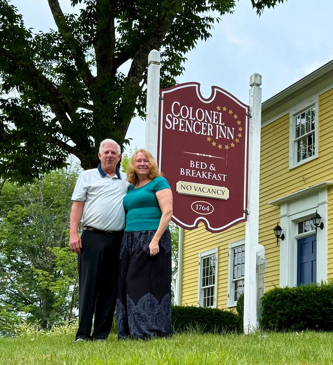 A man and woman are posing for a picture in front of a sign for the colonel spencer inn.