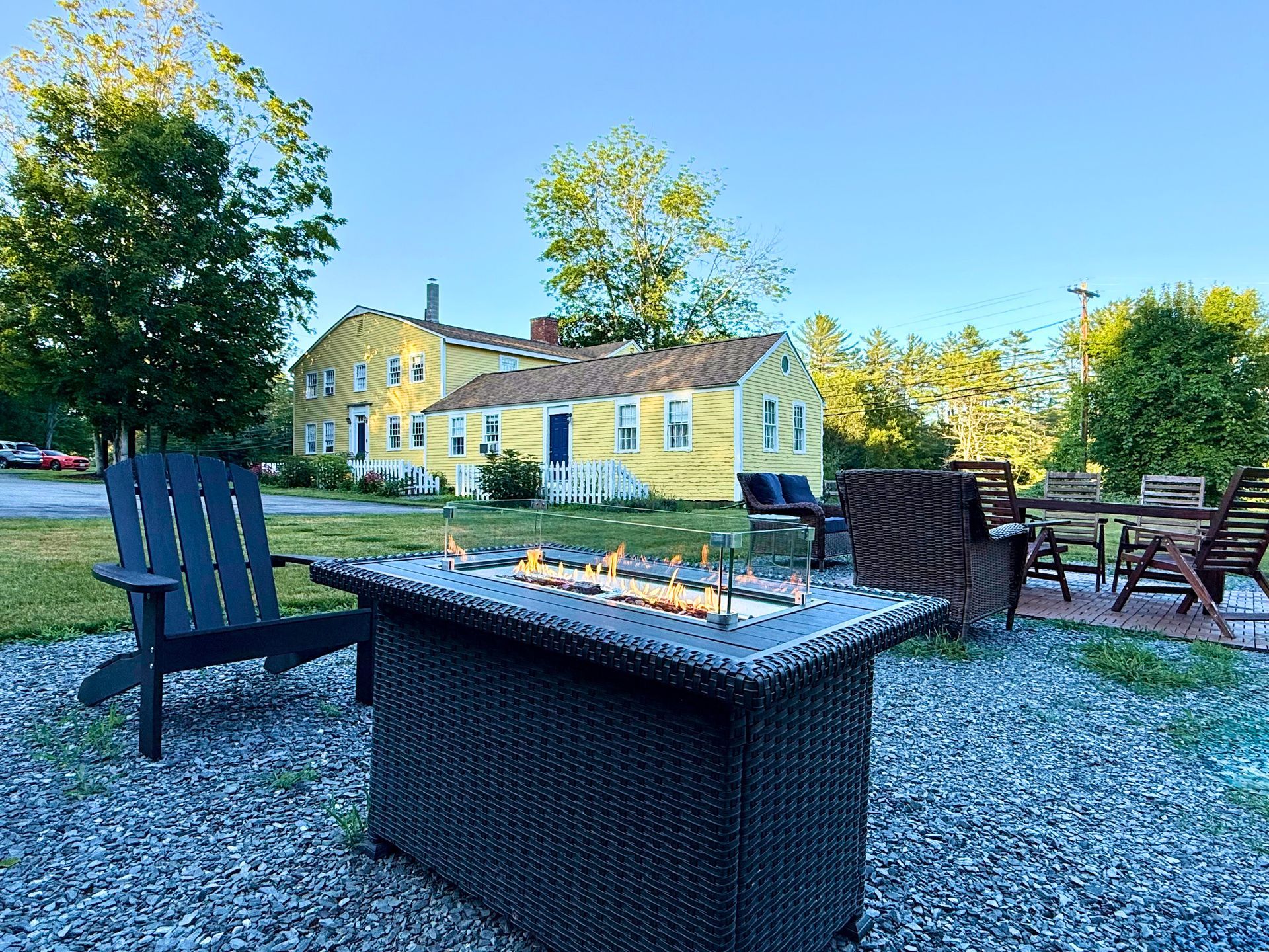 A fire pit with chairs and a table in front of a yellow house.