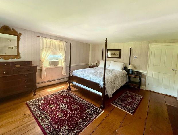 A bedroom with a four poster bed , dresser , mirror and rug.