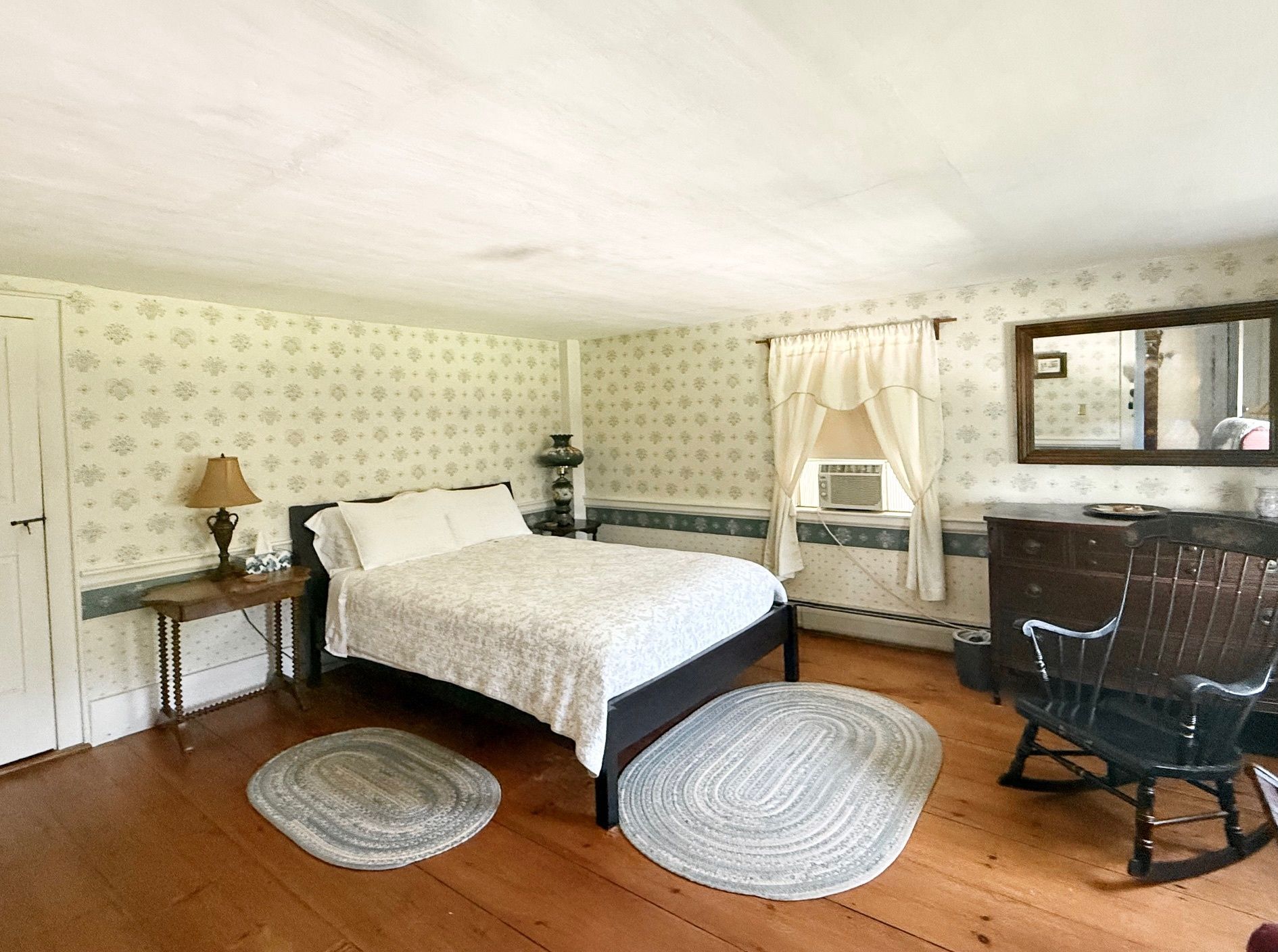 A bedroom with a bed , rocking chair , dresser and mirror.
