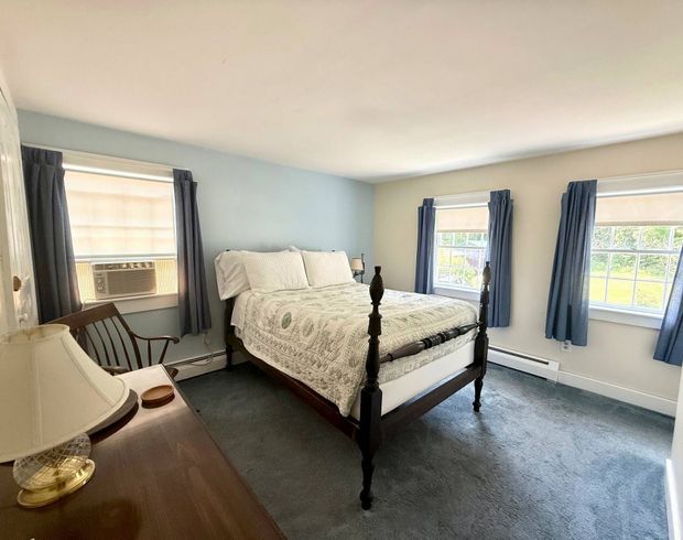 A bedroom with a bed , dresser , chair , lamp and windows.