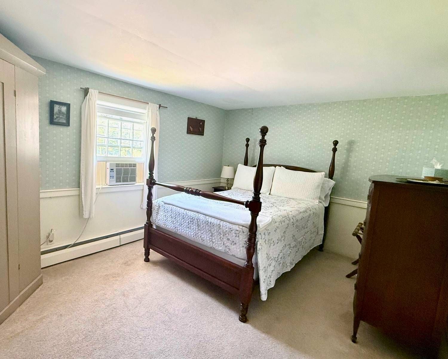 A bedroom with a four poster bed , dresser , and window.