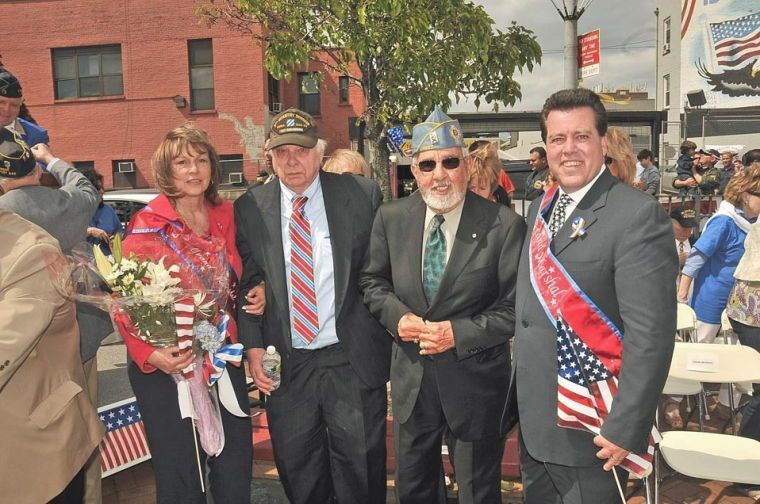 A group of people posing for a picture with one man wearing an american flag sash