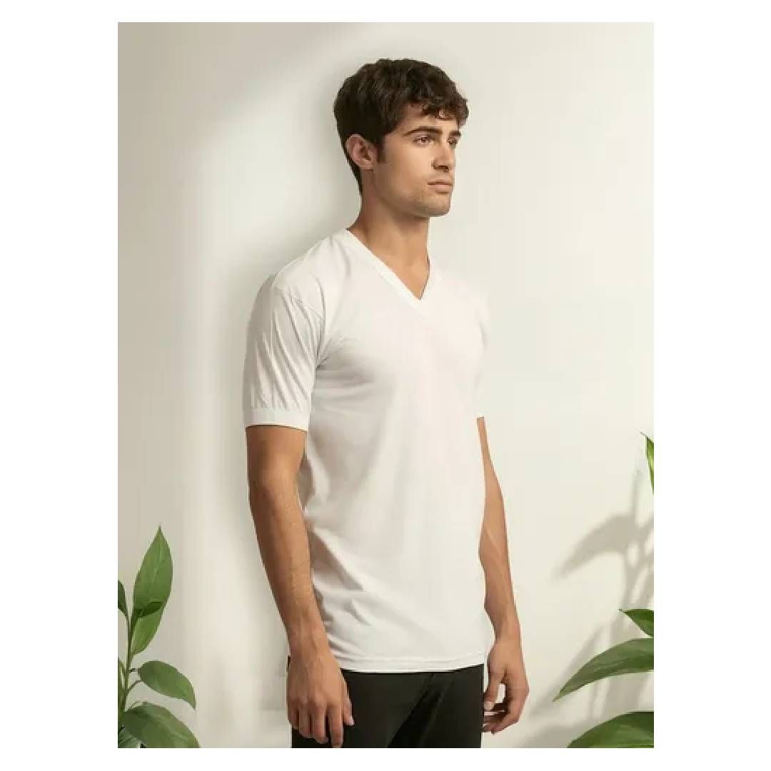 Un hombre que lleva una camiseta blanca con cuello en V está parado junto a una planta.