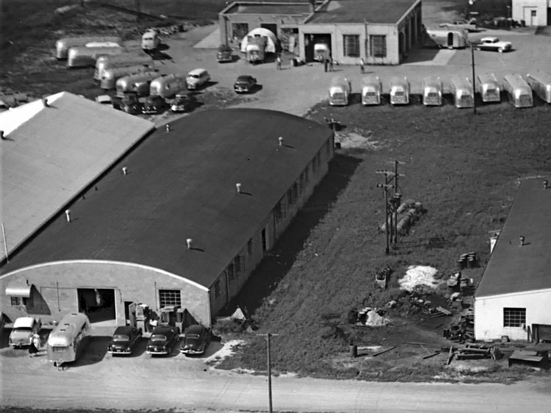 A warehouse and workshop with busses in a lot around the workshop