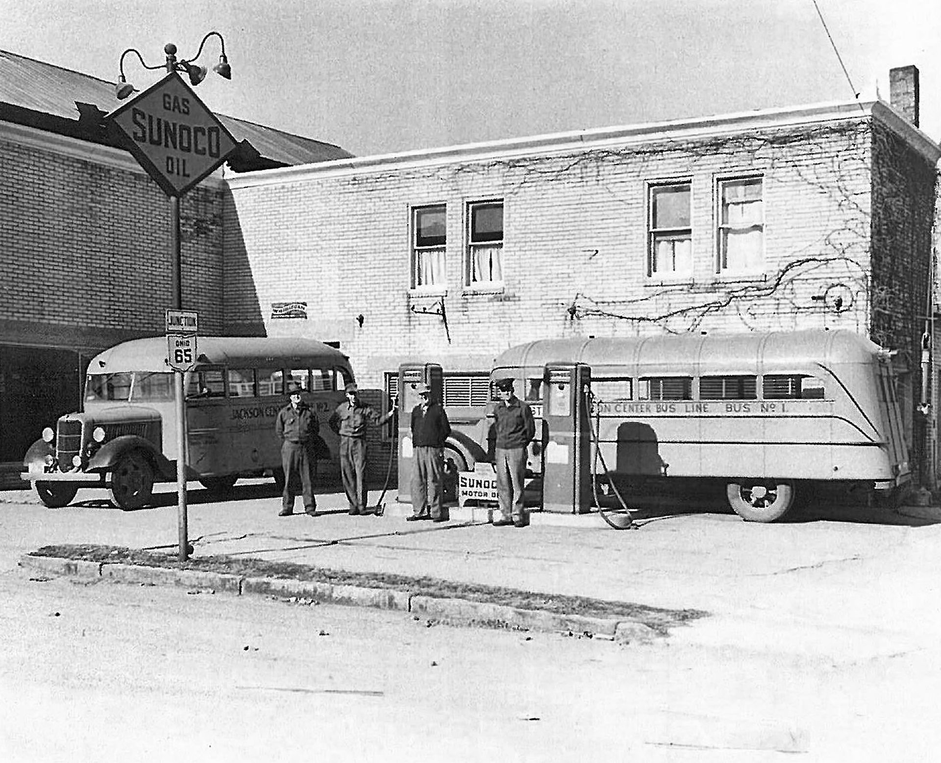 4 men refilling their busses with gas at the gas station.