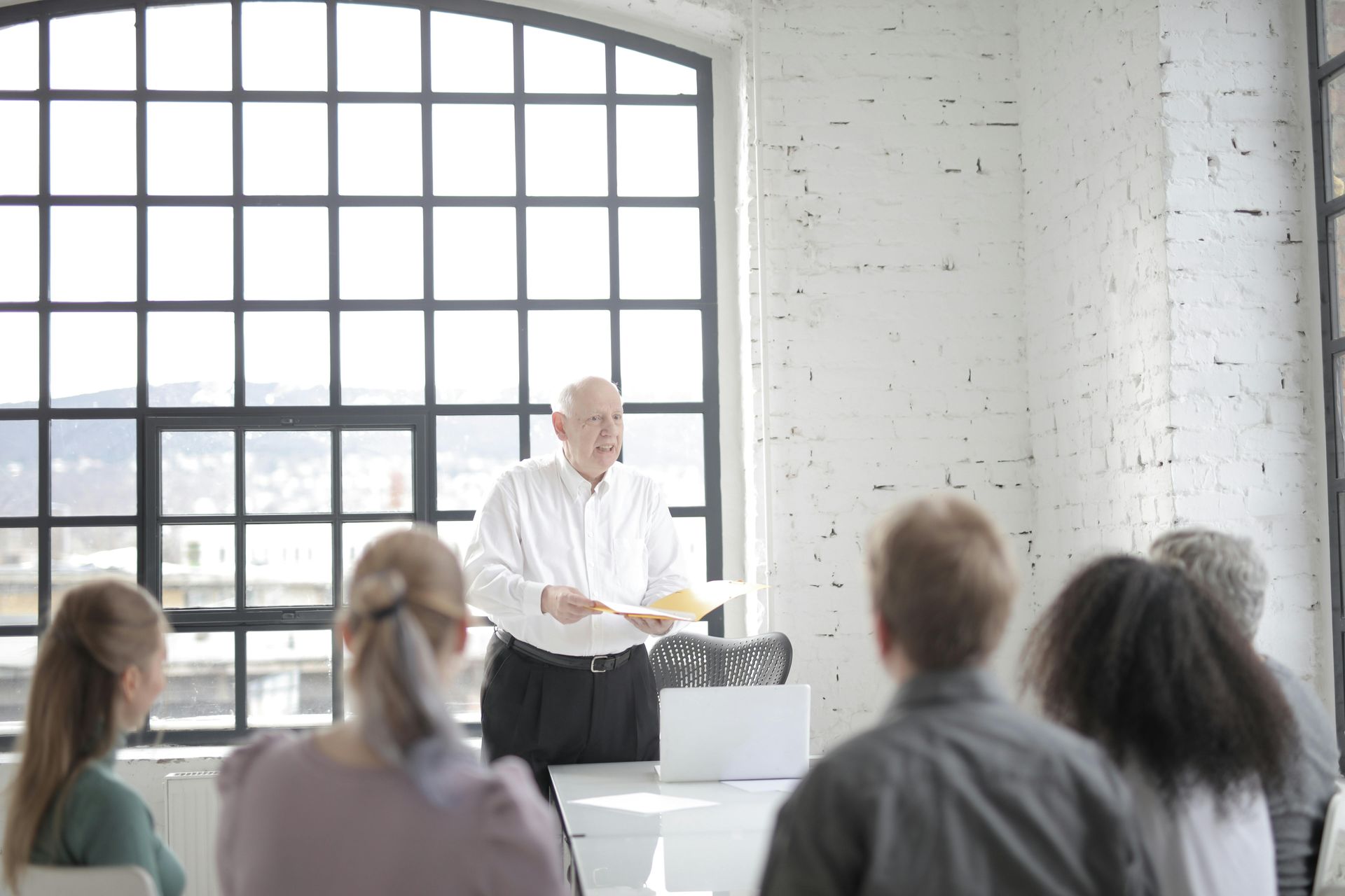 A person stands at the head of a table holding a document, presenting to a small group of people in a bright, modern office.