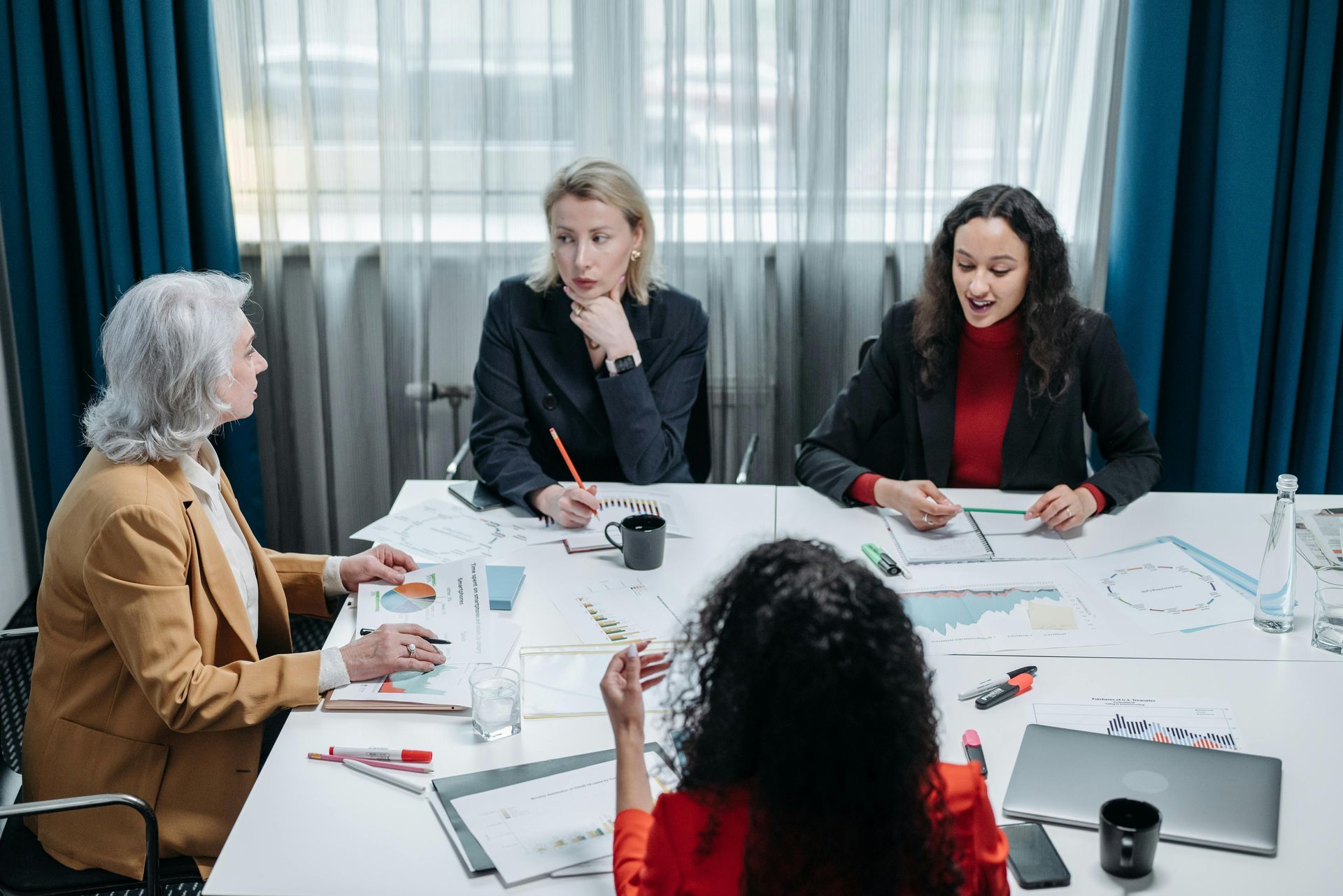 Four people sit around a white conference table in an office, reviewing documents and discussing business.