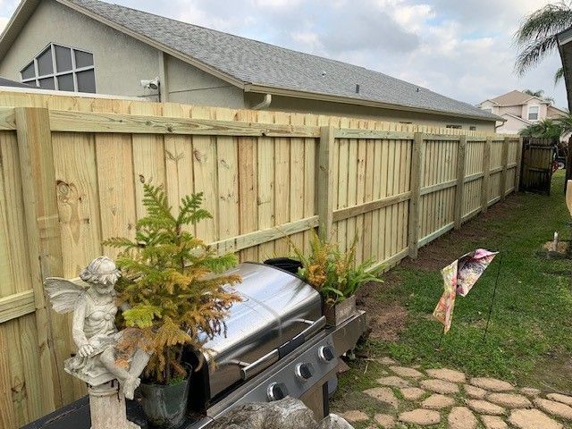 Wooden fence in a backyard with a grill and decorative plants, next to a house.