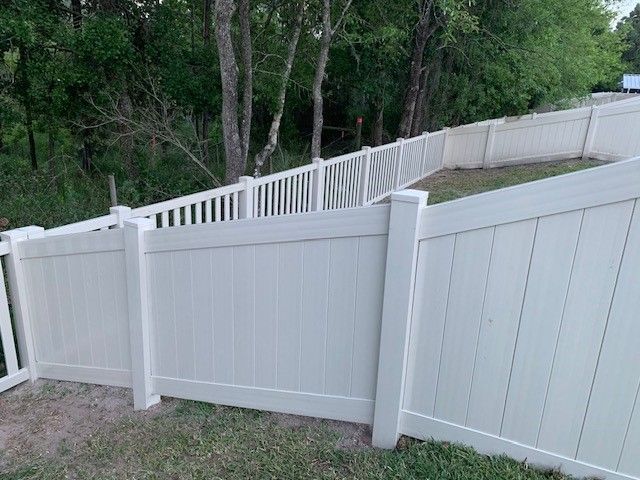 White vinyl fence in a yard, surrounded by trees.