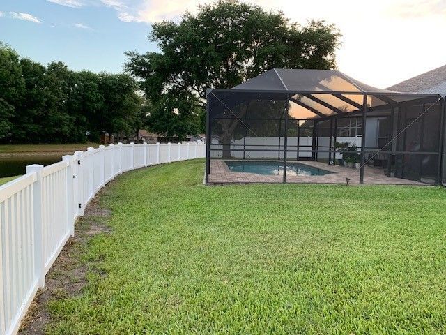White fence curves around a green lawn, leading to a screened pool area.