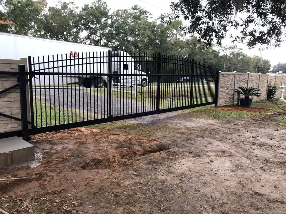 Black metal gate and fence in front of a gravel driveway. A semi truck is parked behind the fence.
