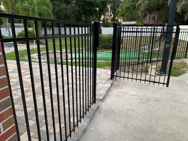 Black metal fence with open gate, leading to a mini golf course.