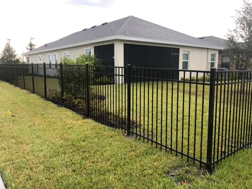 Black metal fence surrounding a backyard with a beige house and green grass.