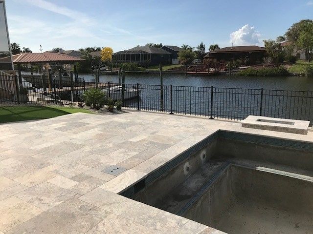 Patio with empty pool overlooking a canal, black fence, houses, sunny day.