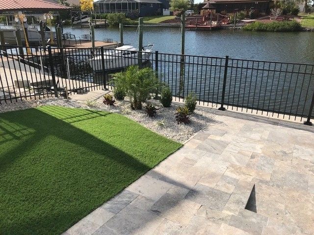 Backyard with artificial turf, stone patio, black fence, and water view.