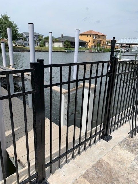 Black metal fence on a wooden dock, waterfront view with houses in the background.
