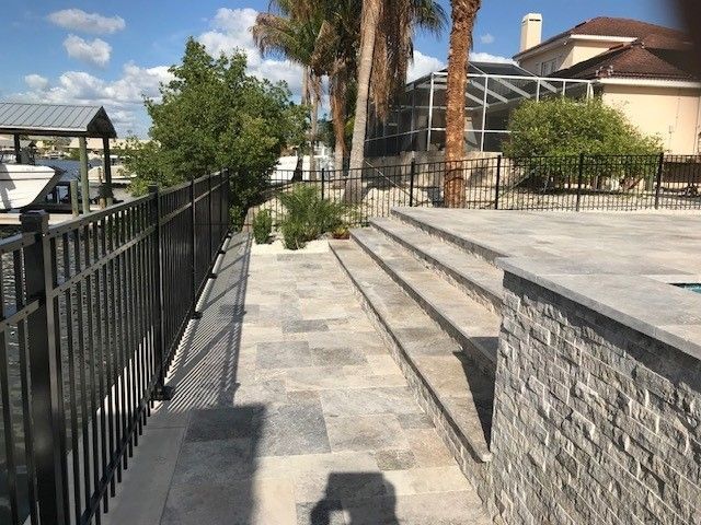 Stone path with steps leads to a pool area, black fencing and water views. Sunny day.