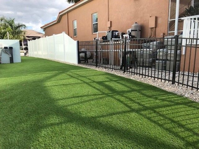 Green artificial turf yard with a white fence and black metal fence.