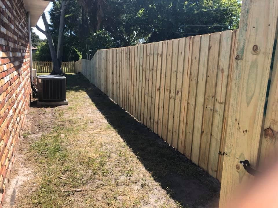 Wooden fence along a brick building and grass, in a sunny outdoor setting.