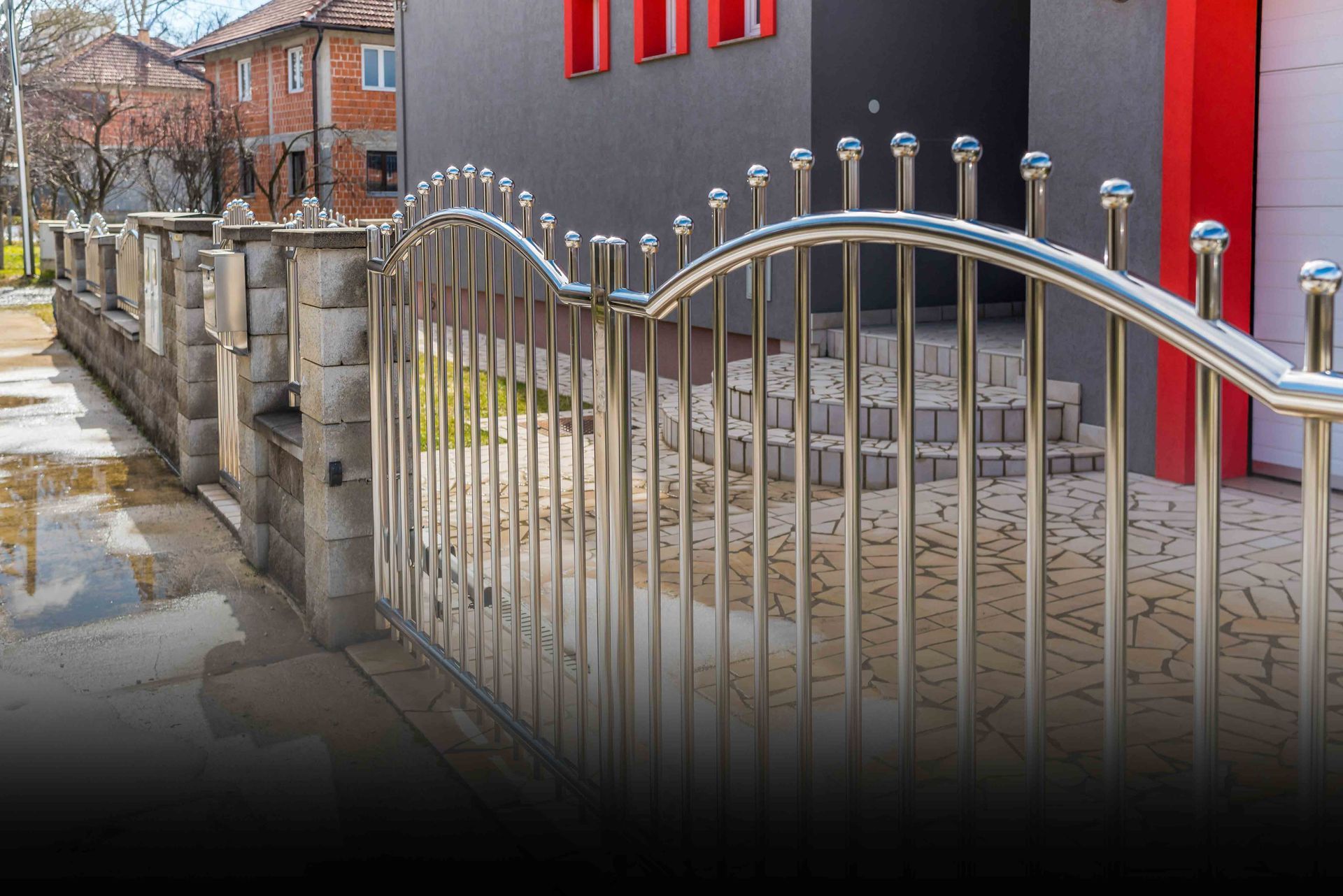 Stainless steel gate and fence with a concrete wall in front of a dark gray house.