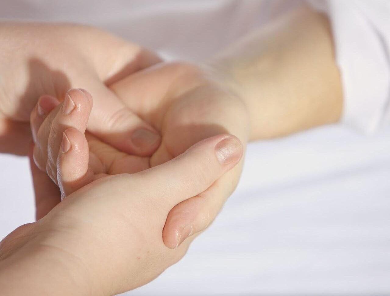 Hands giving a wrist massage, likely for pain relief. Light skin, white background.