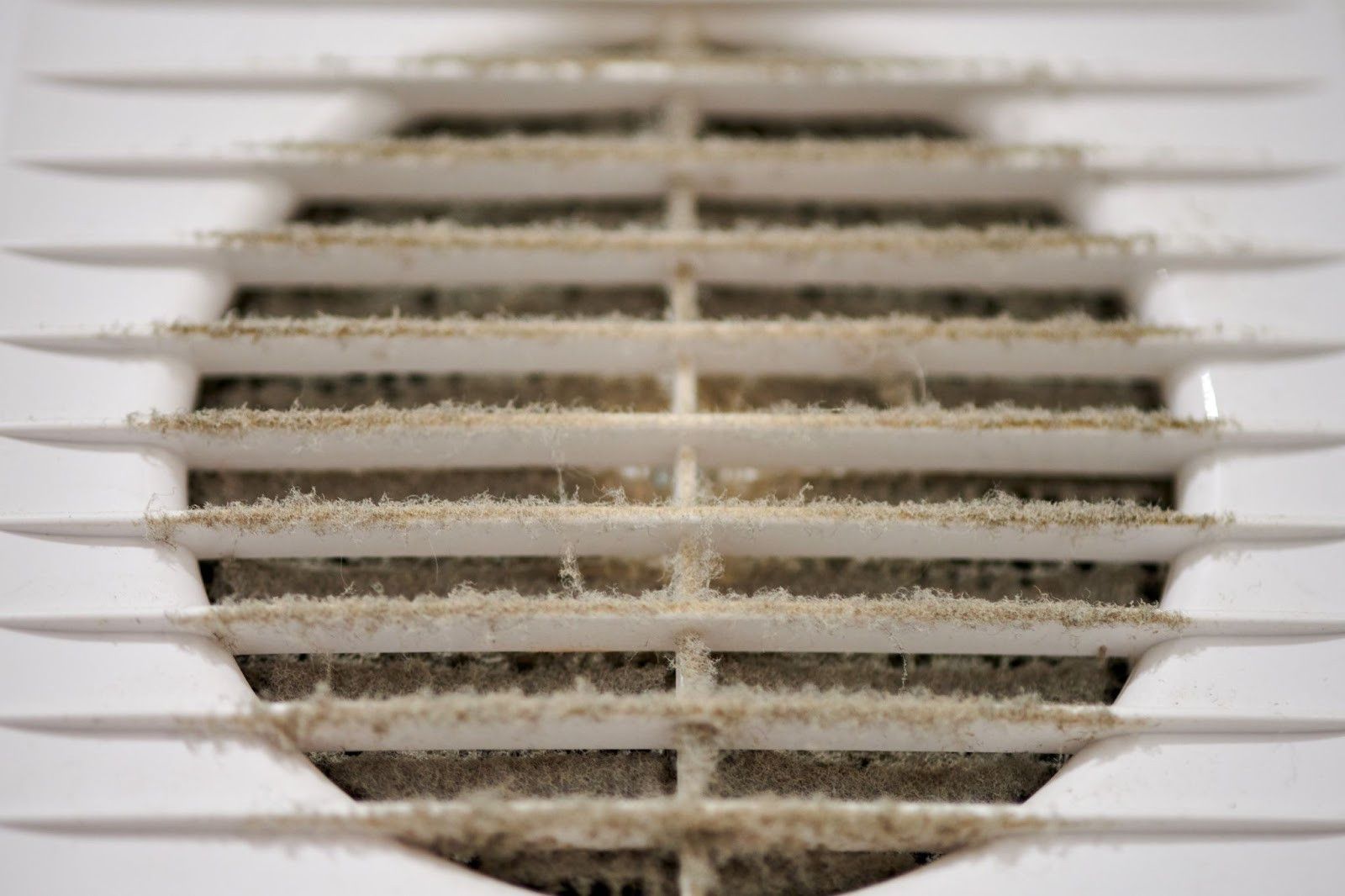 A close up of a dirty air vent on a wall.