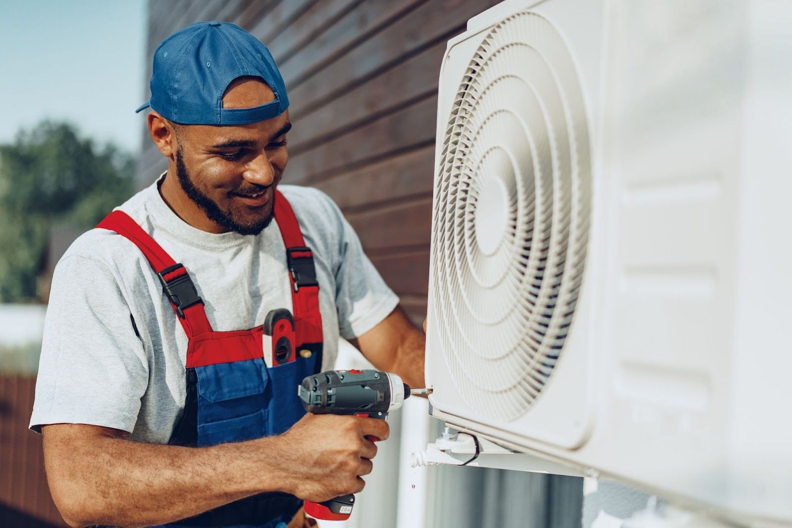 A man is fixing an air conditioner with a drill.