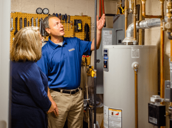 A man and a woman are standing next to a water heater.