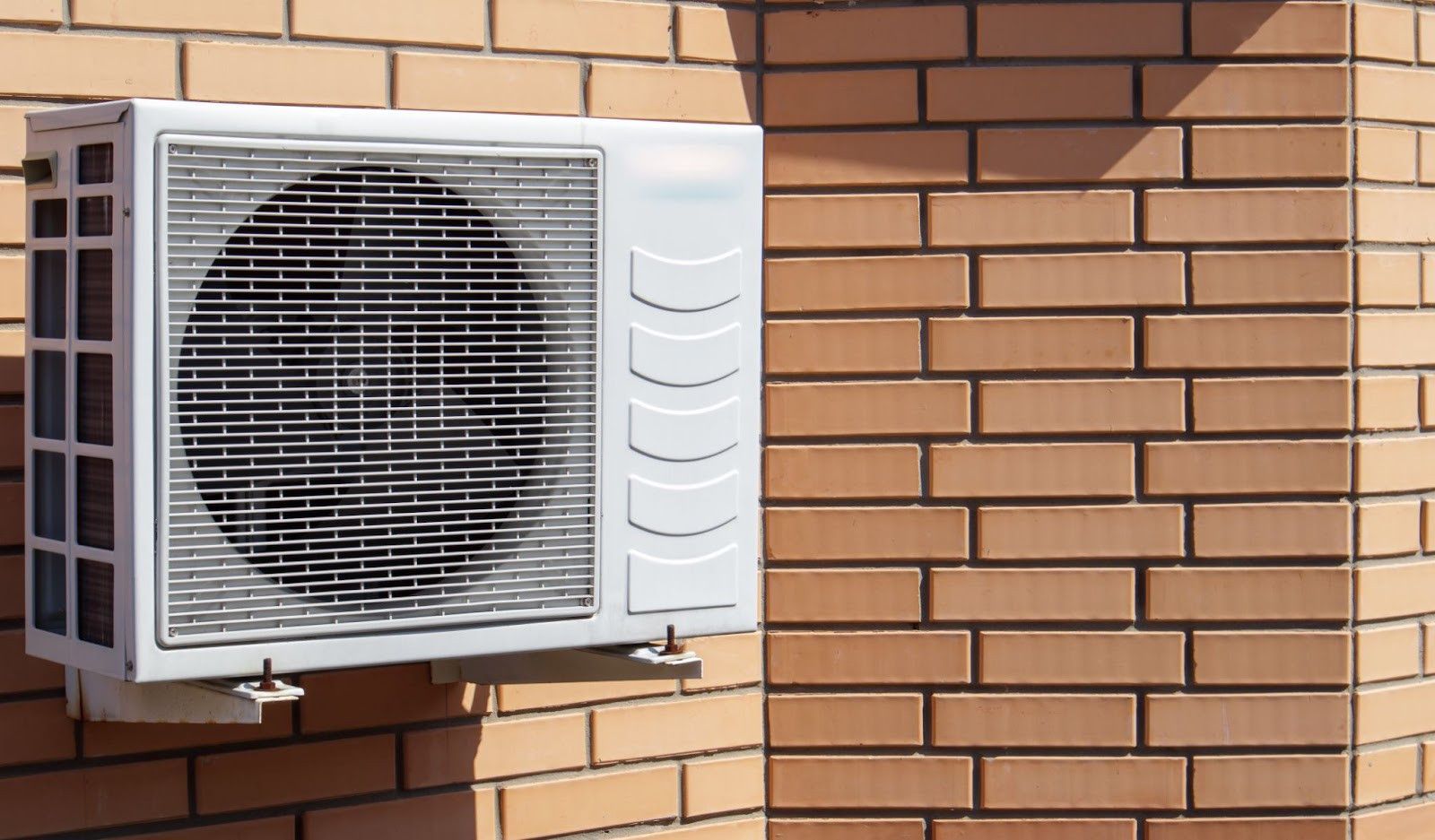 A white air conditioner is mounted on a brick wall.