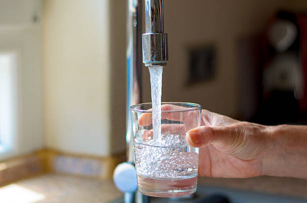 A person is pouring water into a glass from a faucet.