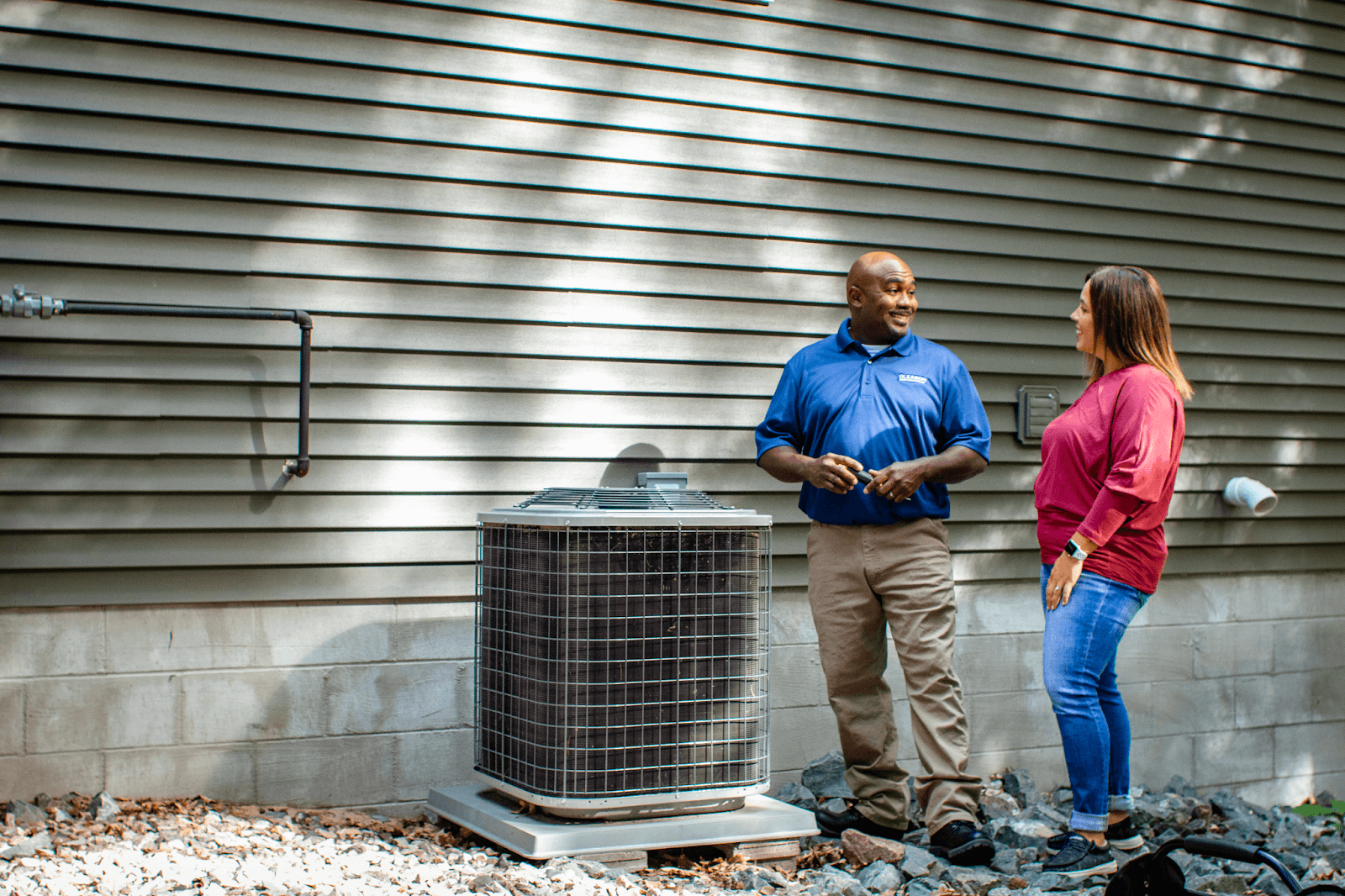 A man and a woman are standing next to an air conditioner outside of a house.