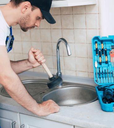 A man is using a plunger to fix a kitchen sink - Plumbing