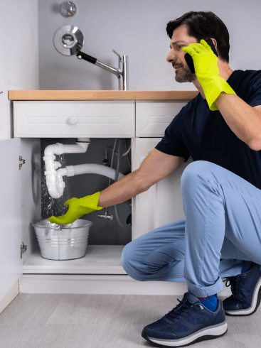 A man is kneeling under a sink while doing Plumbing