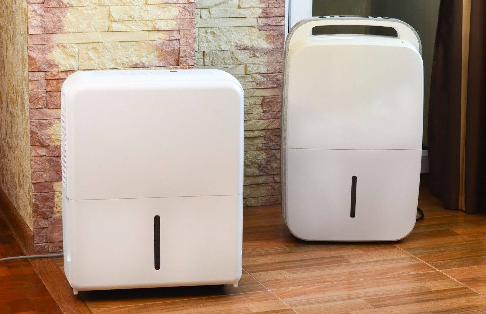 Two white dehumidifiers are sitting next to each other on a wooden floor in a room.