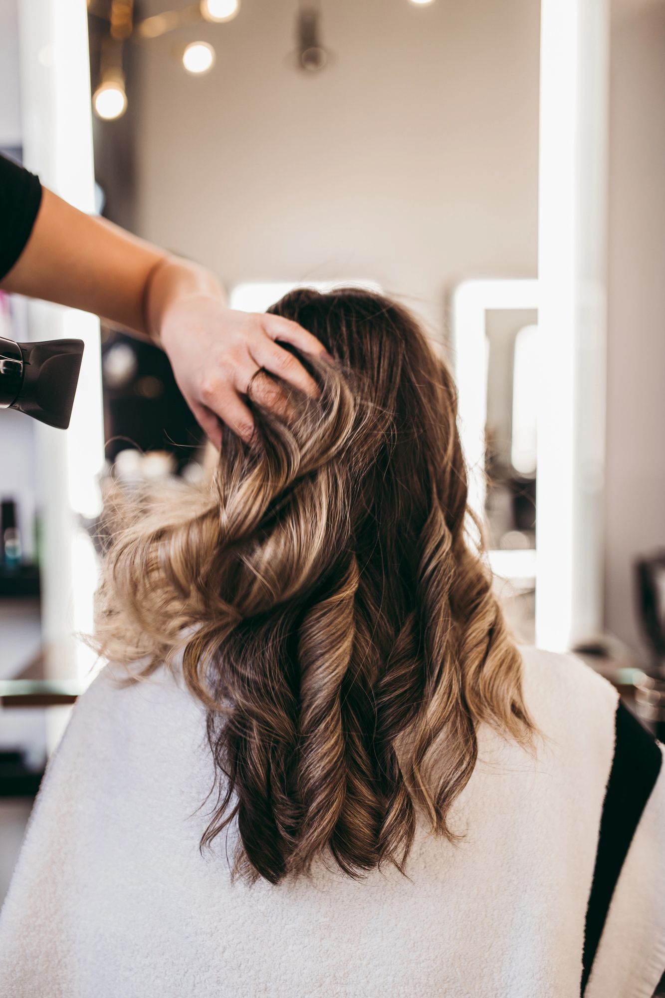 Estilista rizando el cabello ondulado castaño y rubio de una mujer en el salón.