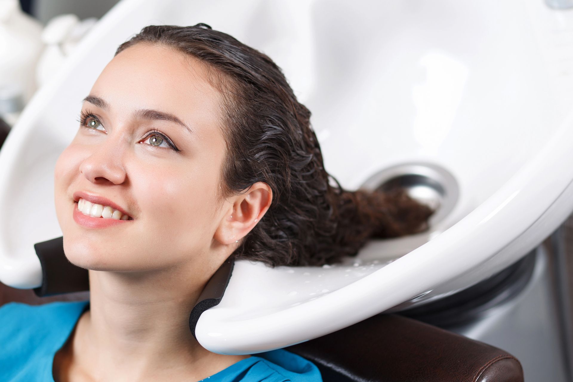 Mujer con el cabello mojado sonriendo en el lavabo de un salón de belleza, recibiendo un lavado de cabello.