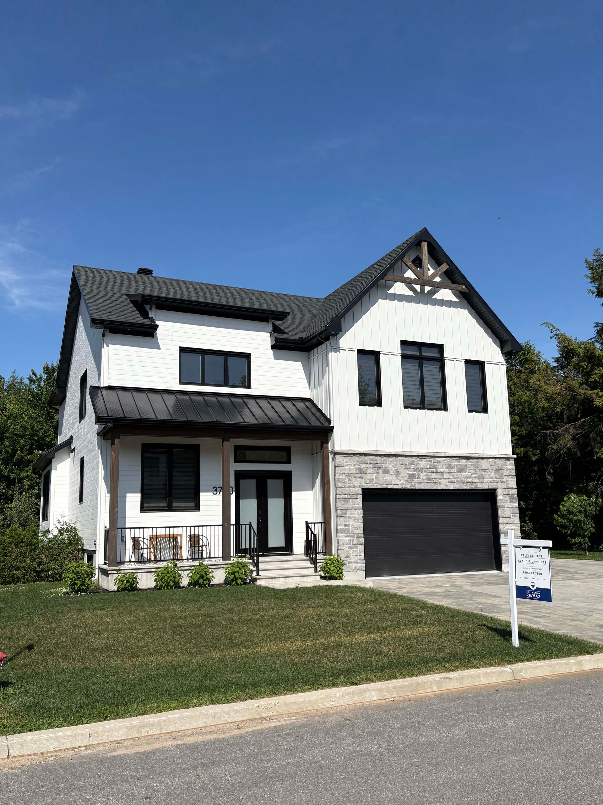 Une grande maison blanche avec une porte de garage noire est à vendre.