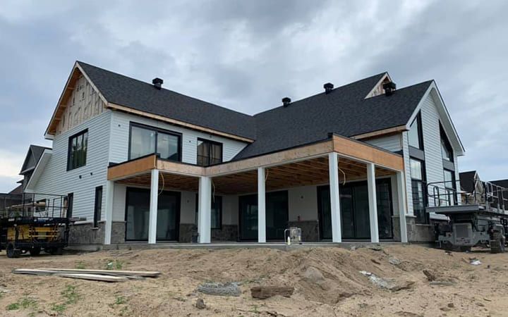 Une grande maison blanche avec un toit noir est en construction.