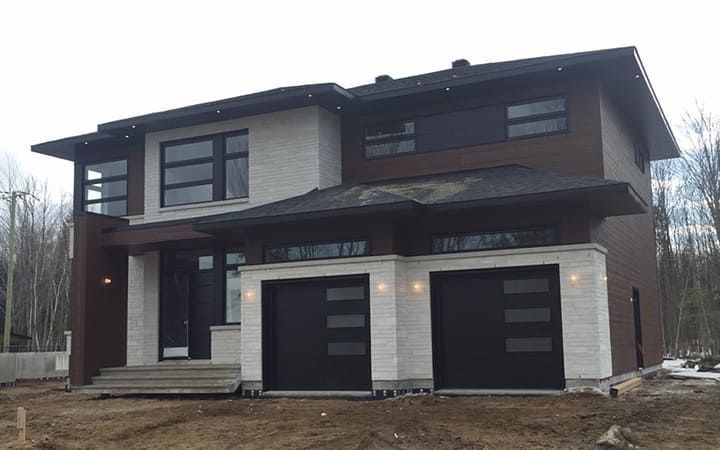 Une grande maison avec deux portes de garage est située au sommet d'un champ de terre.