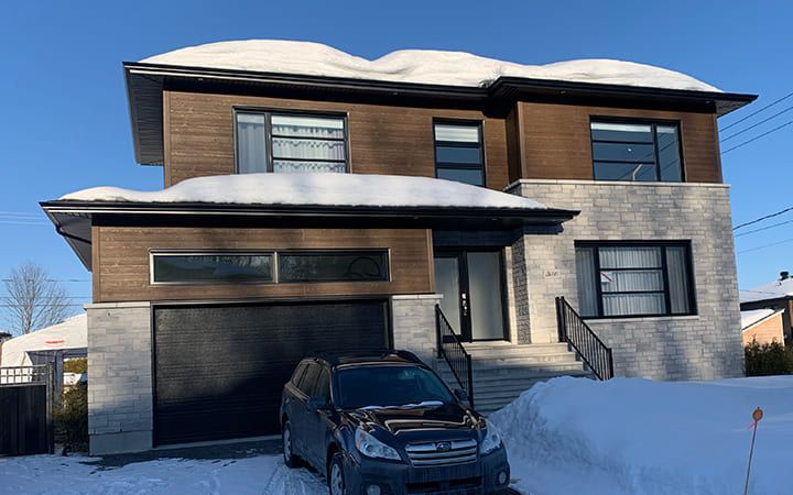Une voiture est garée devant une grande maison recouverte de neige.