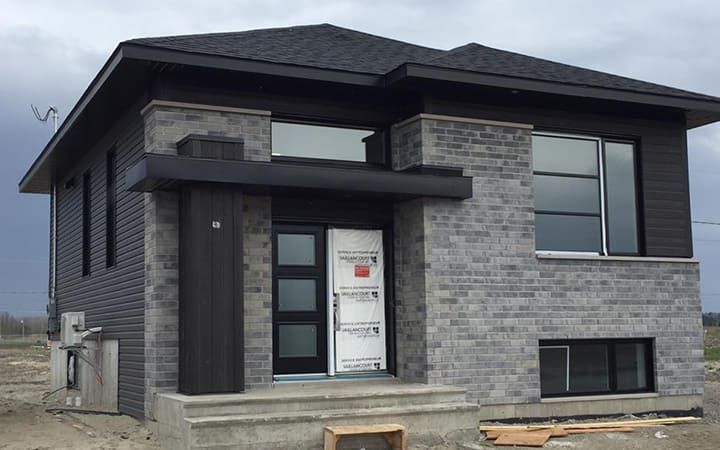 Une maison en briques avec un toit noir est en construction.