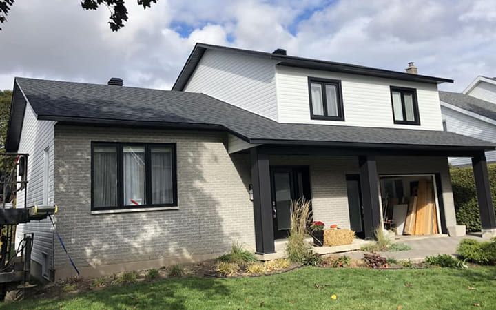 Une grande maison blanche avec un toit noir est située au sommet d'une colline verdoyante.