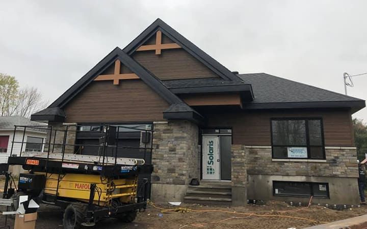 Un élévateur à ciseaux jaune est garé devant une maison en construction.